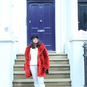 Red faux fur coat white jeans outside bright blue dor